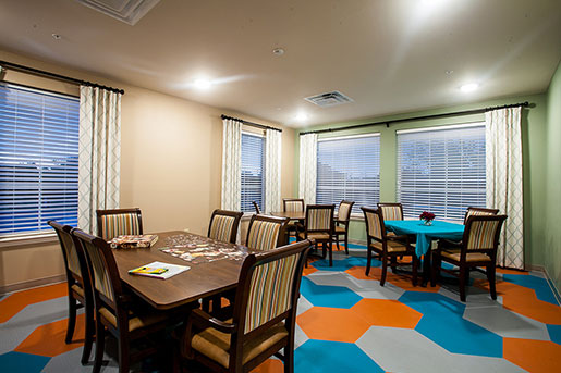 Bright communal dining area with wooden tables and colorful geometric flooring.