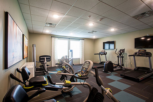 Modern fitness room with treadmills, exercise bikes, and wall-mounted TVs.