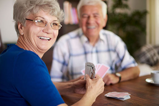 Two older adults enjoying a card game at a table in a communal area.