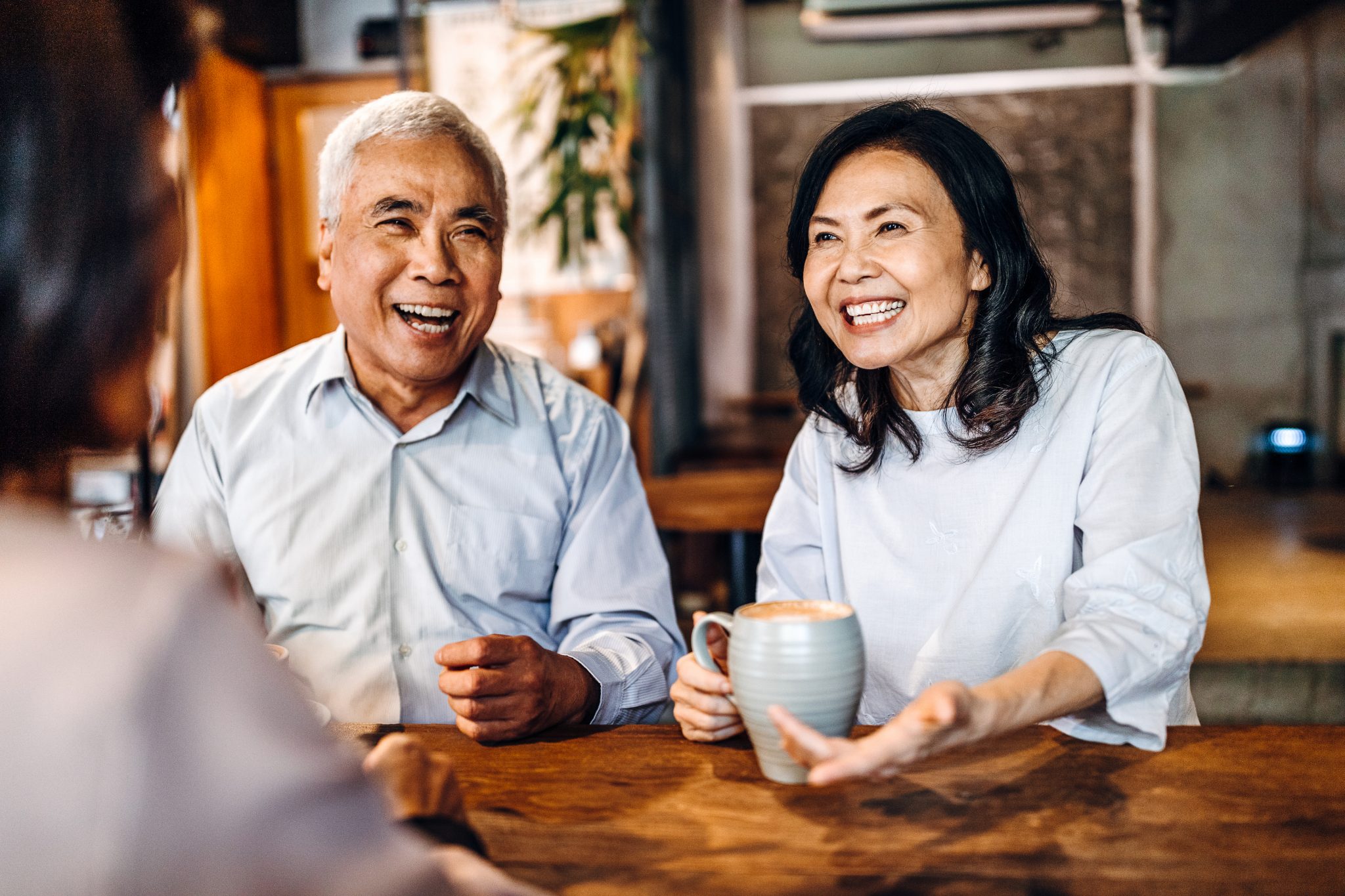 Two smiling seniors enjoying conversation at a wooden table indoors.