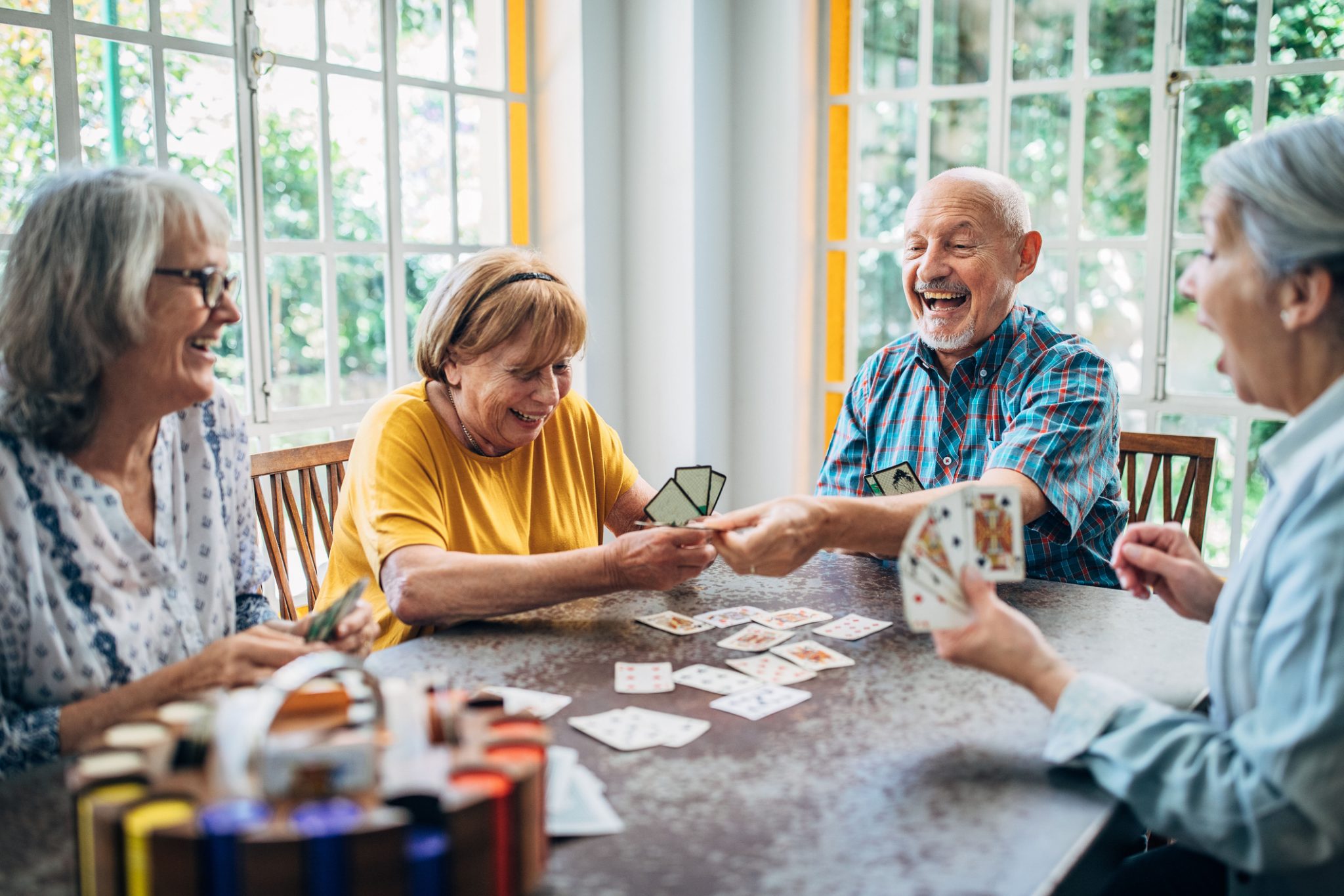 Group of seniors enjoying a game of cards together, laughing around a table in a bright room.