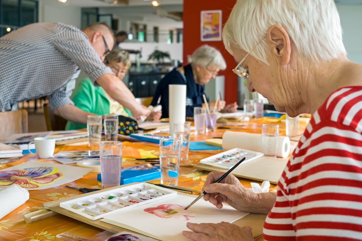 Seniors engaging in a vibrant painting class with colorful palettes on an orange tablecloth.