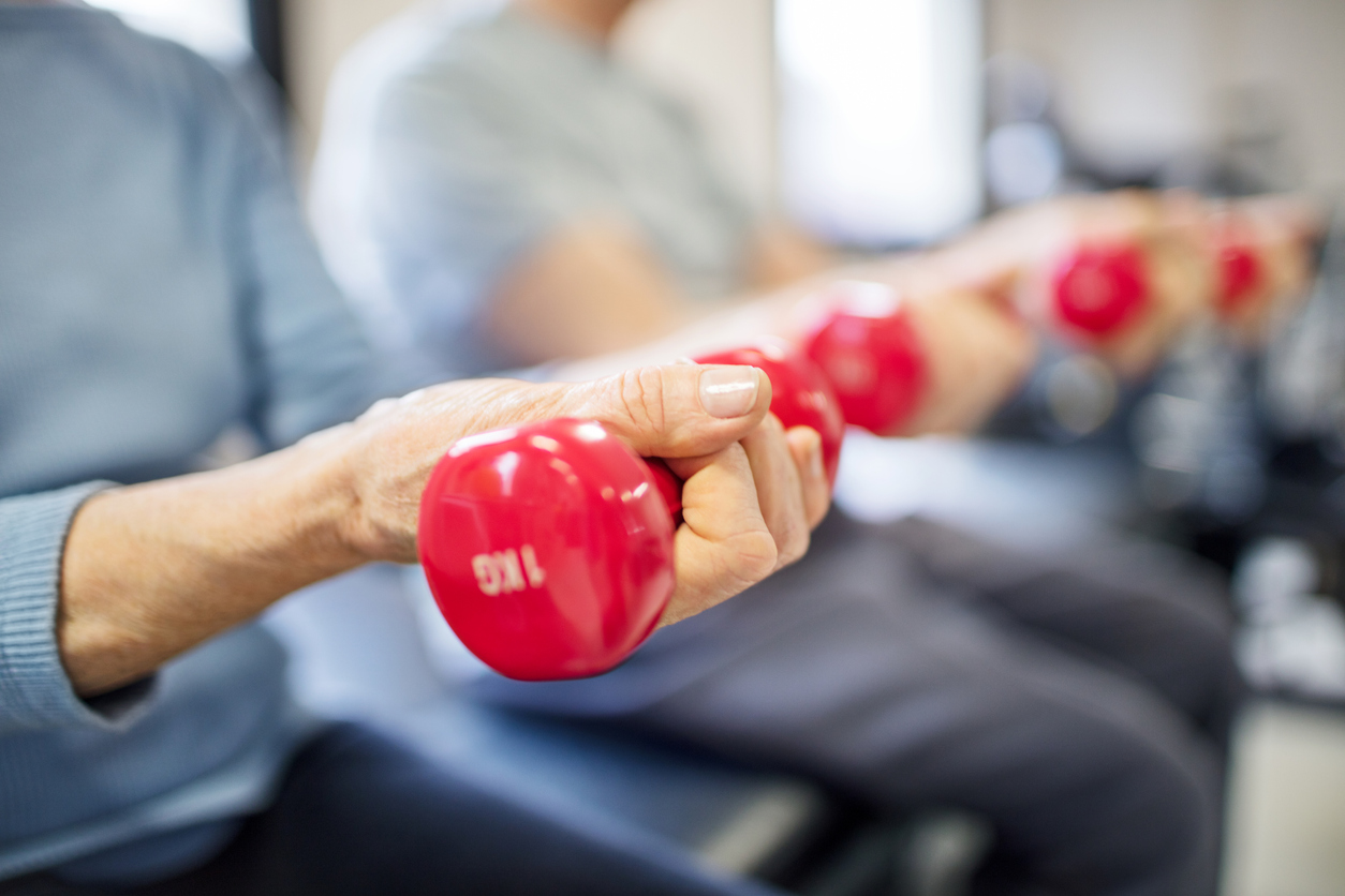 Close-up of seniors exercising with red dumbbells during a fitness class.