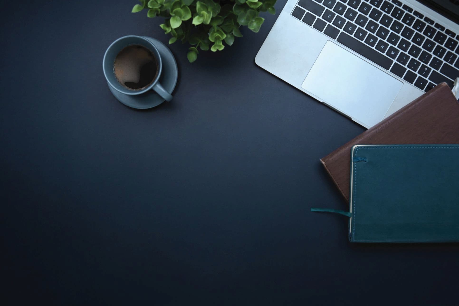 Close up of dark desk with computer, coffee, and notebooks