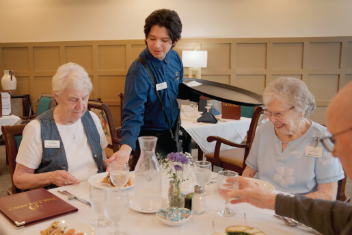 Server dropping off dishes to a group of dining seniors