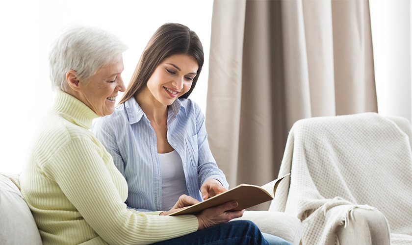 Senior woman sitting with adult daughter looking through photo album